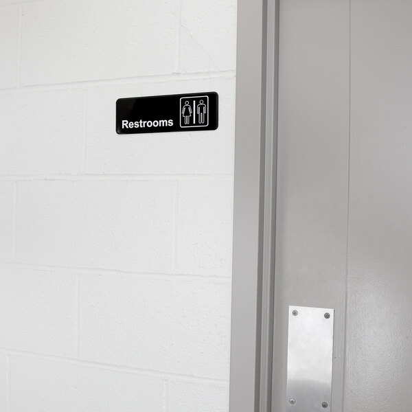 A Vollrath Traex restroom sign on a white wall.