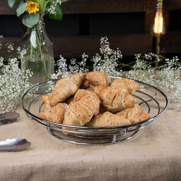 A Clipper Mill chrome plated iron wire basket filled with croissants on a table.