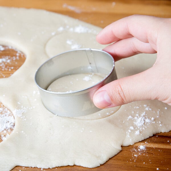 A person using an Ateco metal circle cookie cutter to cut dough.