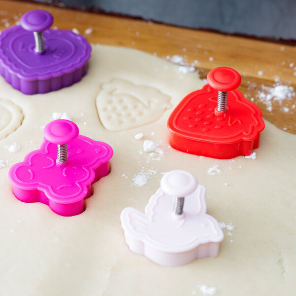 A 4-piece Ateco plastic cookie cutter set on dough with red and white plunger tops.