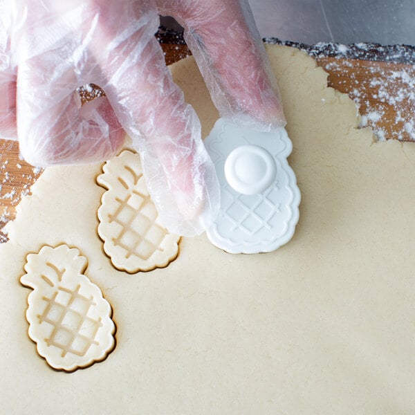 A person using an Ateco plastic pineapple pastry cutter to cut out a pineapple shape in cookie dough.