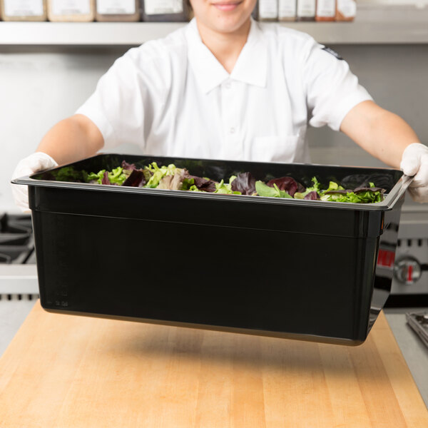 A woman holding a black Cambro food container filled with salad.