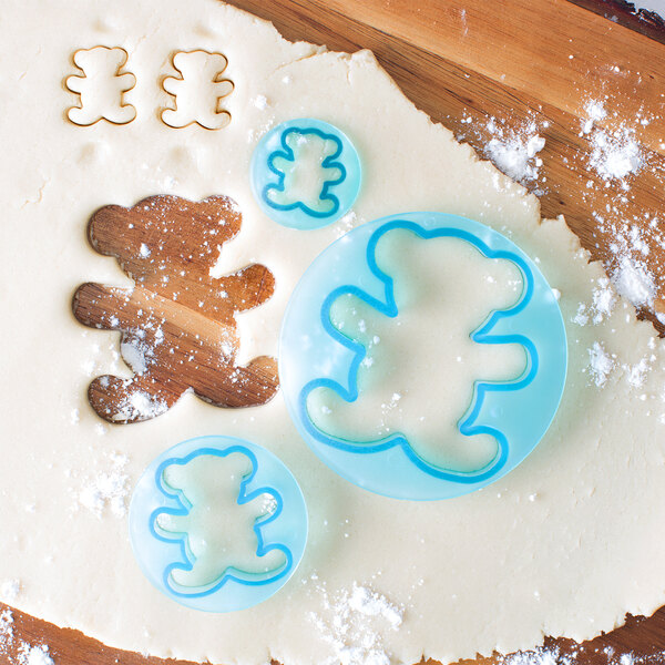 A cookie dough with a bear shape cut out using Ateco blue plastic teddy bear cookie cutters.