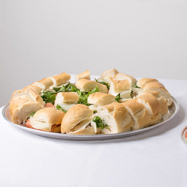A Durable Packaging round foil catering tray on a table with sandwiches and salad.