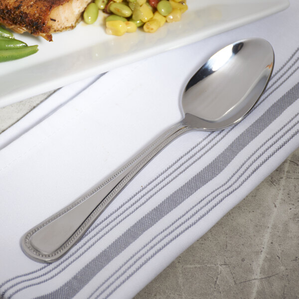 A 10 Strawberry Street Pearl stainless steel serving spoon on a white plate with food.