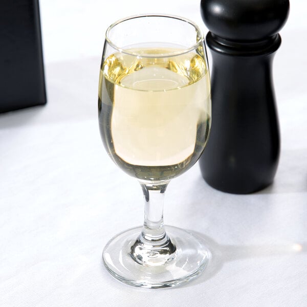 A Libbey white wine glass filled with white wine next to a salt and pepper shaker.