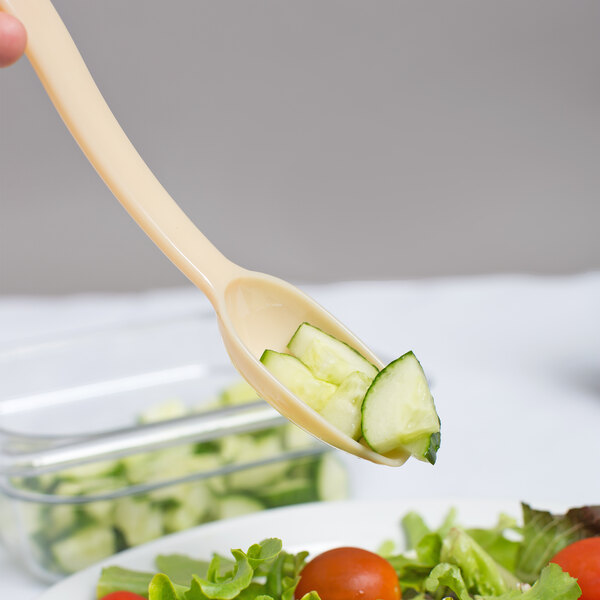A Cambro beige Camwear salad bar spoon filled with cucumber slices.