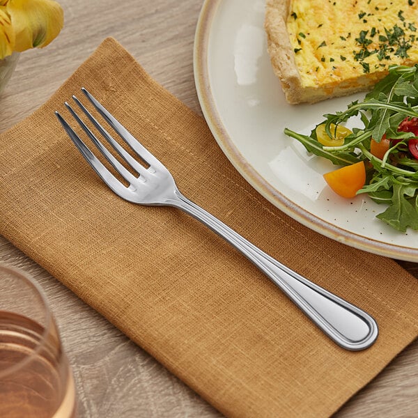 An Acopa Edgeworth stainless steel table fork on a plate with food.