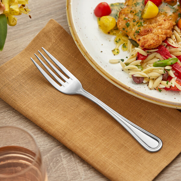 A plate of food on a napkin with an Acopa Edgeworth stainless steel dinner fork.
