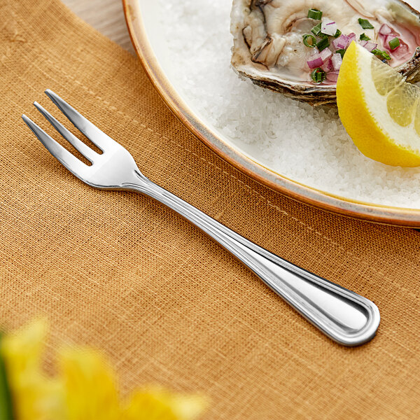 An Acopa stainless steel oyster fork on a plate with a piece of oyster.
