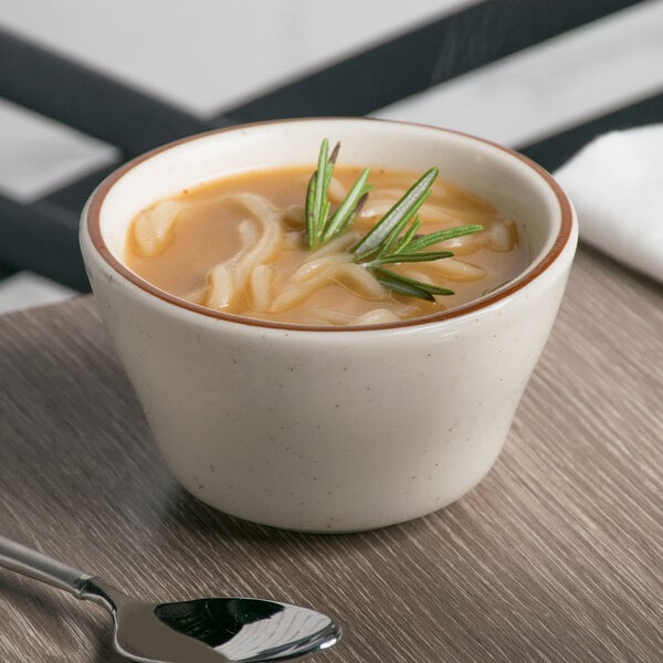 A Tuxton brown speckle china bouillon bowl filled with soup and a sprig of rosemary on top.
