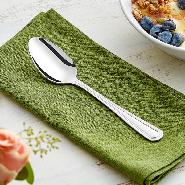 An Acopa Landsdale stainless steel teaspoon on a green napkin next to a bowl of food with blueberries.