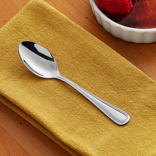 An Acopa Edgewood stainless steel teaspoon on a napkin next to a bowl of strawberries.