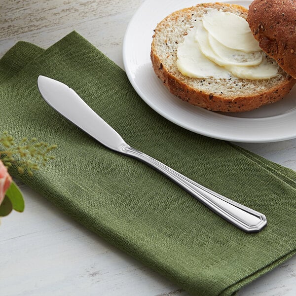 An Acopa stainless steel butter knife on a plate with bread and butter.