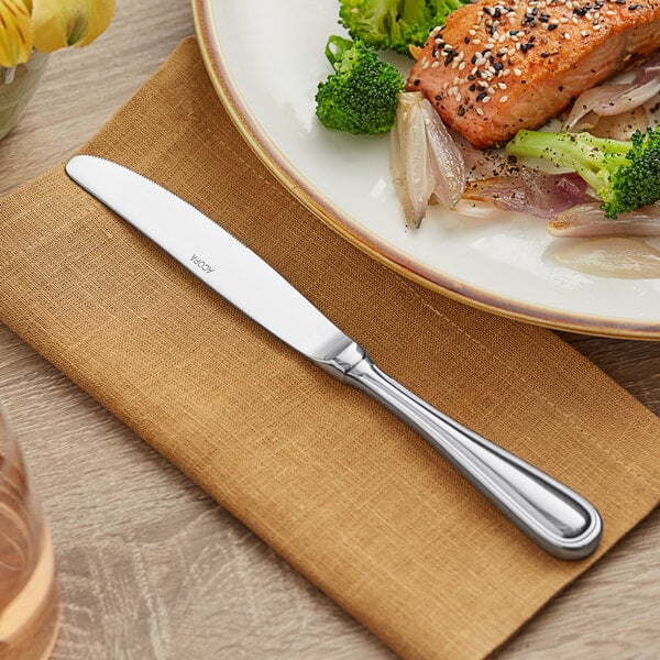 A plate of meat and broccoli with an Acopa Edgeworth stainless steel dinner knife on a napkin