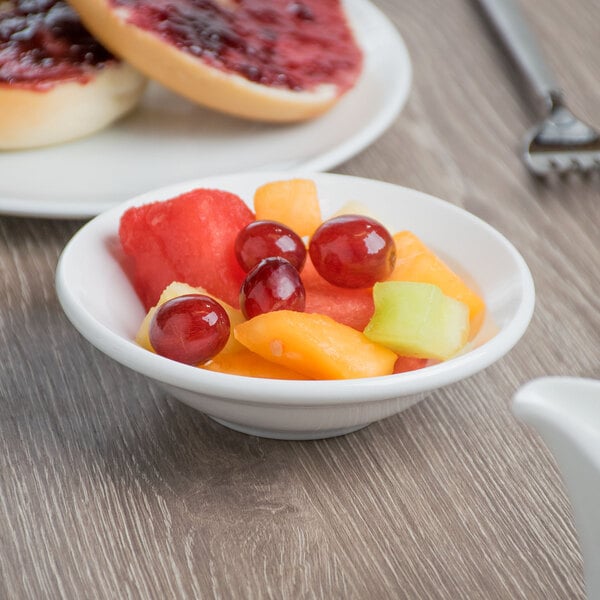 A Libbey Basics bright white porcelain fruit bowl filled with fruit on a table.