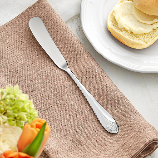 An Acopa stainless steel butter spreader on a napkin next to a plate of bread.