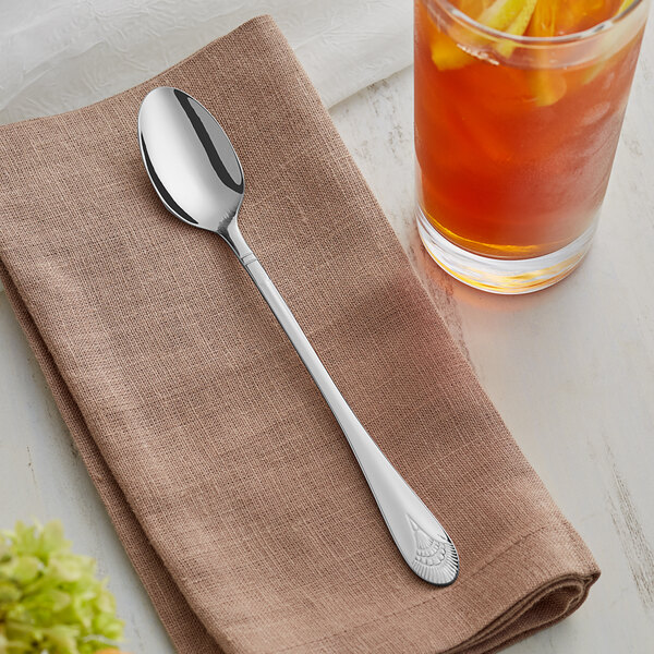 An Acopa Monaca stainless steel iced tea spoon on a napkin next to a glass of liquid.