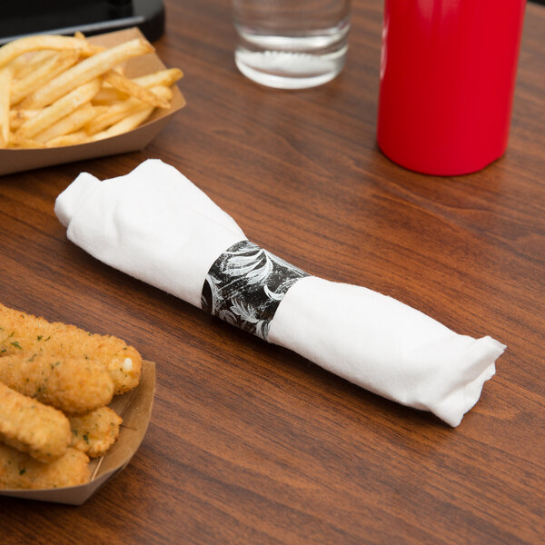 A Hoffmaster white linen-like napkin and clear plastic cutlery set wrapped in a napkin on a table with french fries and a red cup.