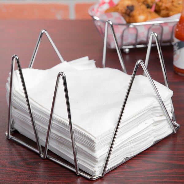 A stack of napkins in a Clipper Mill chrome plated wire napkin holder.