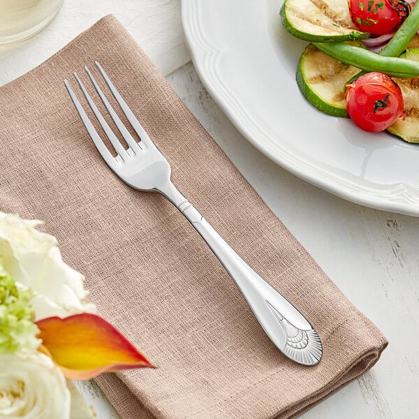 An Acopa Monaca stainless steel dinner fork on a napkin next to a plate of food.