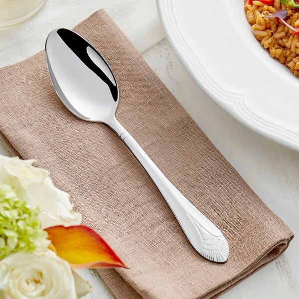 An Acopa Monaca stainless steel serving spoon on a napkin next to a bowl of food.