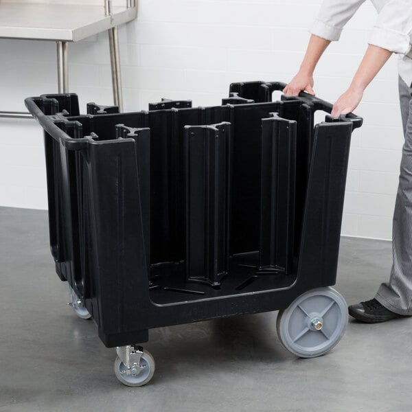 A person pushing a black plastic Cambro dish caddy.
