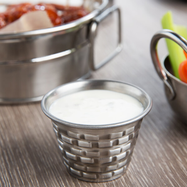 A Tablecraft stainless steel sauce cup with white sauce next to a bowl of food.