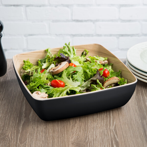 A Tablecraft black melamine bowl filled with salad on a table.