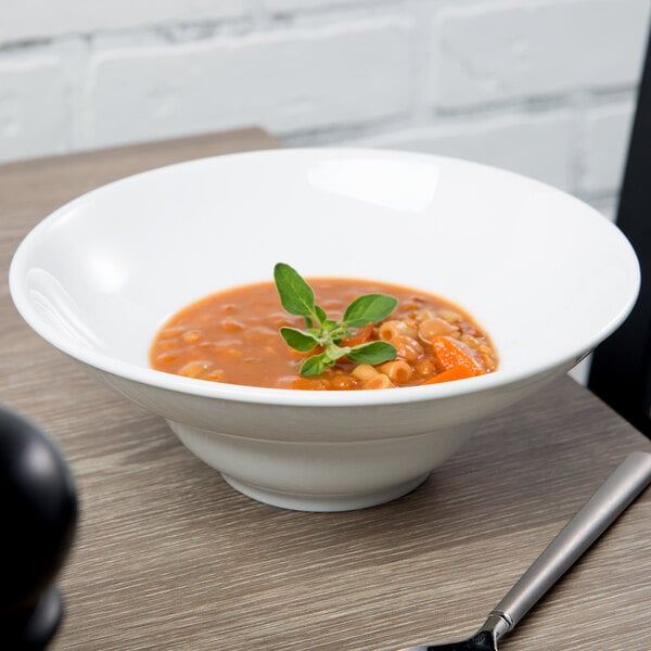 A Libbey ultra bright white china bowl filled with soup and a leafy herb.