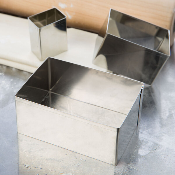 A set of Ateco stainless steel rectangular cookie cutters in a metal box on a table.