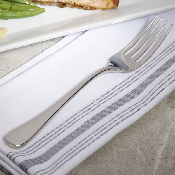 A Bon Chef stainless steel dinner fork on a napkin next to a plate of food.