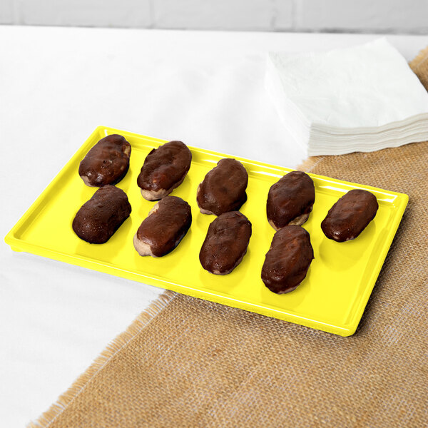 A chocolate covered donut on a yellow Tablecraft rectangular cooling platter.
