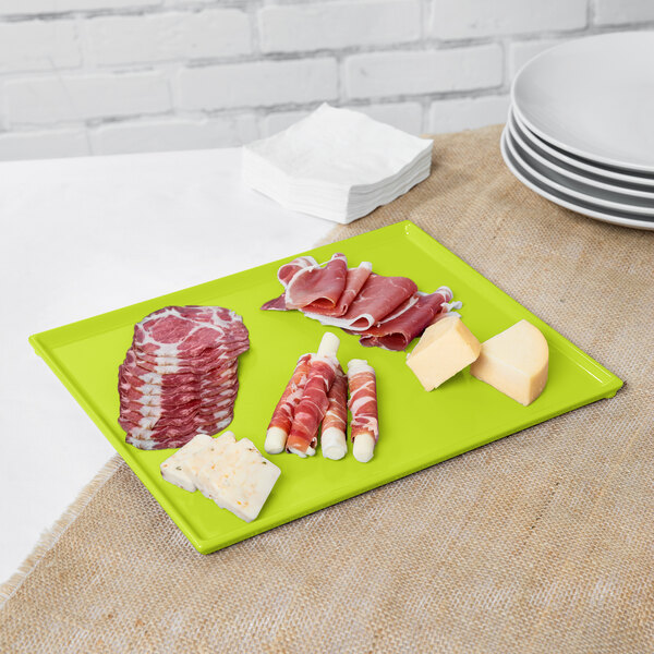 A green Tablecraft cast aluminum platter with meat and cheese on a green surface.