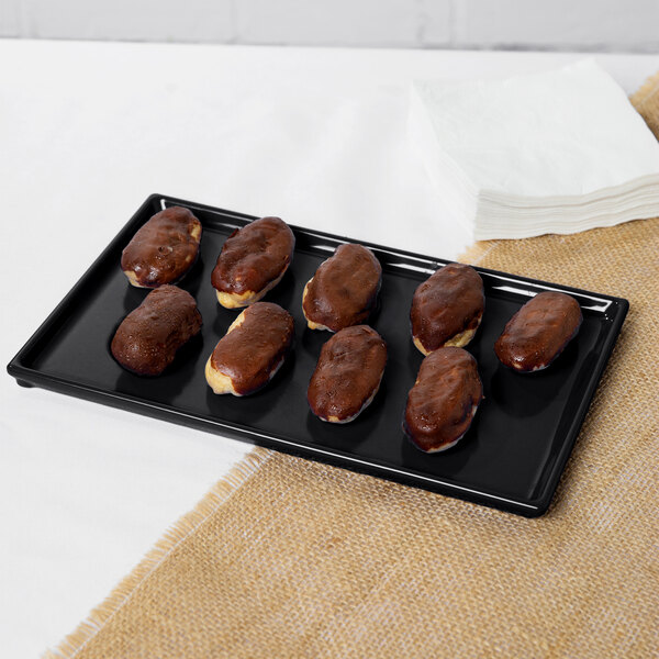 A black Tablecraft cast aluminum rectangular cooling platter with chocolate covered pastries on it.