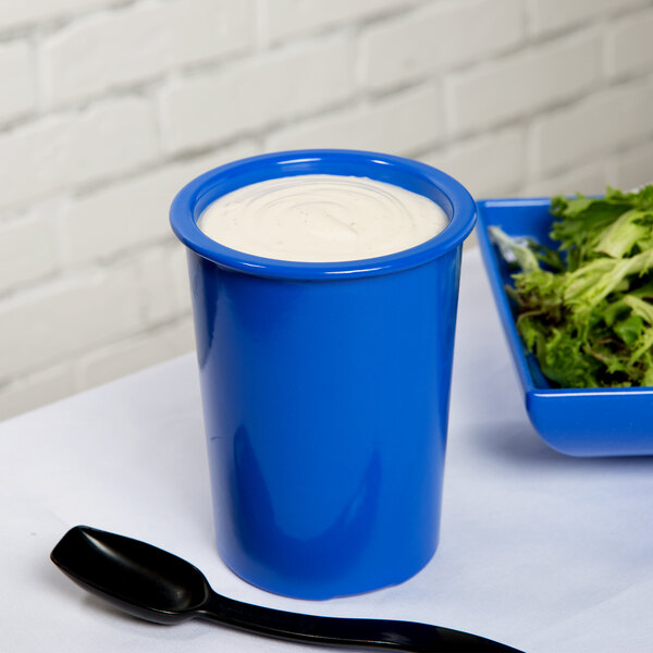 A Tablecraft cobalt blue cast aluminum salad dressing crock filled with white liquid next to a bowl of salad.