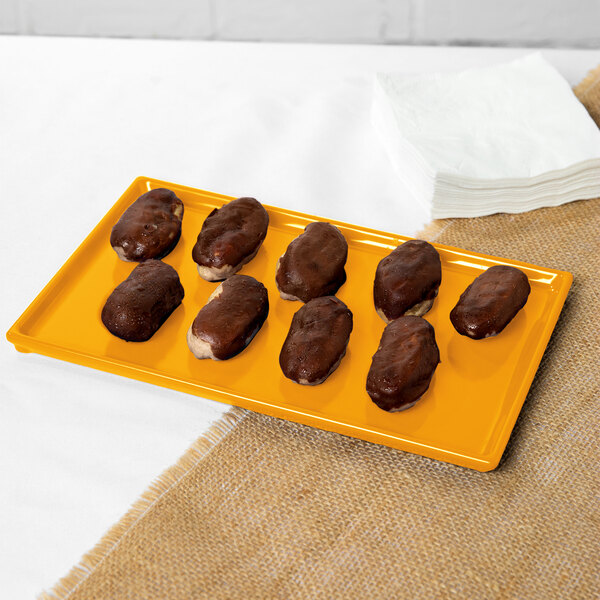 An orange Tablecraft cast aluminum rectangular cooling platter with chocolate covered donuts on it.