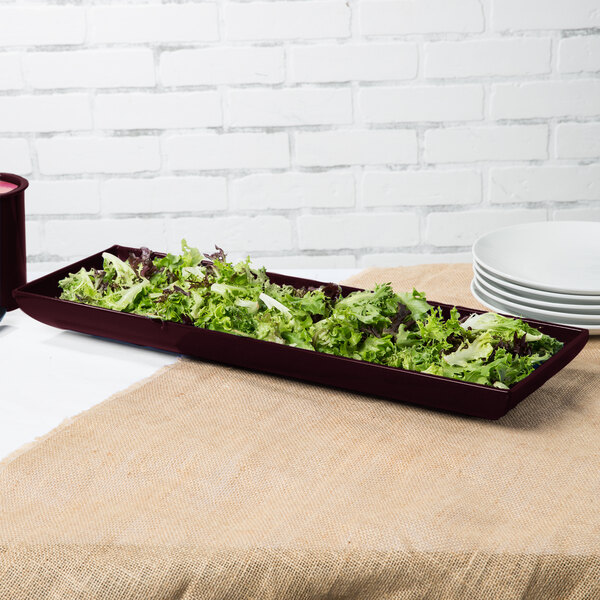 A maroon speckle rectangular platter with a brown container of lettuce on a table.