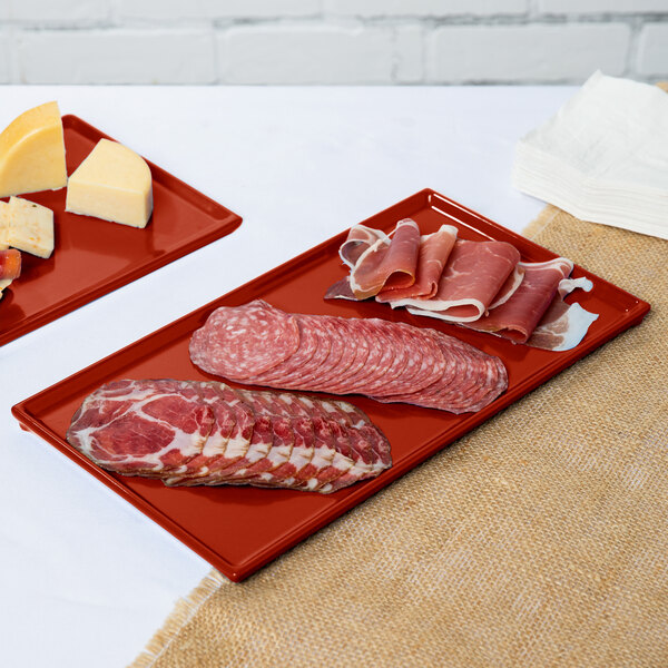 Two Tablecraft copper cast aluminum rectangular cooling platters holding meat and cheese on a counter.