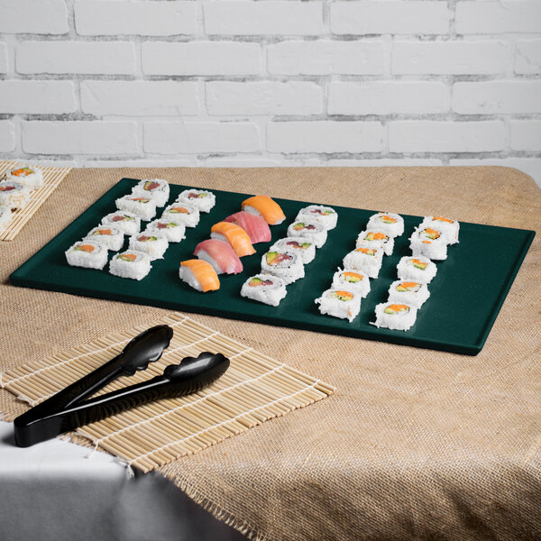 A Tablecraft rectangular cast aluminum cooling platter in hunter green with white speckles on a table with a plate of sushi.