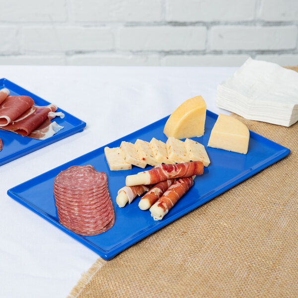Two Tablecraft cobalt blue cast aluminum rectangular cooling platters with meat and cheese on a table.