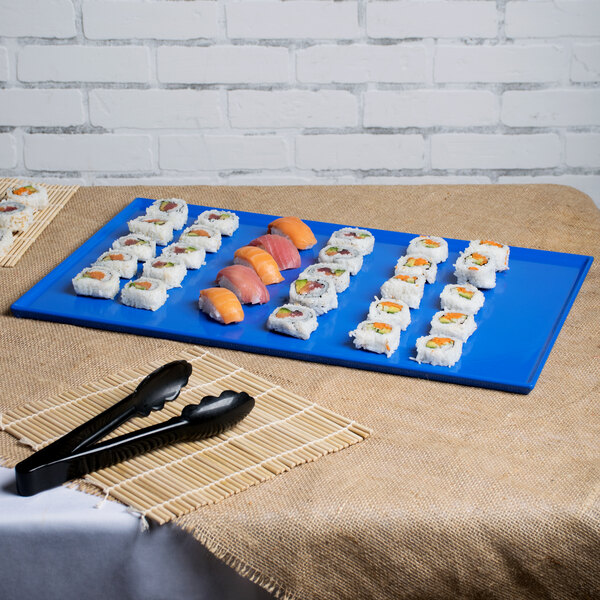 A cobalt blue Tablecraft rectangular cooling platter with sushi on it next to a pair of tongs.