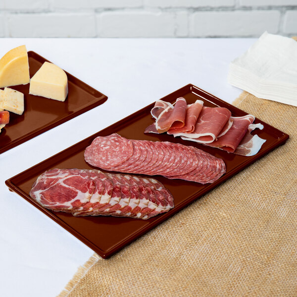 Two brown Tablecraft cast aluminum rectangular trays holding meat and cheese.