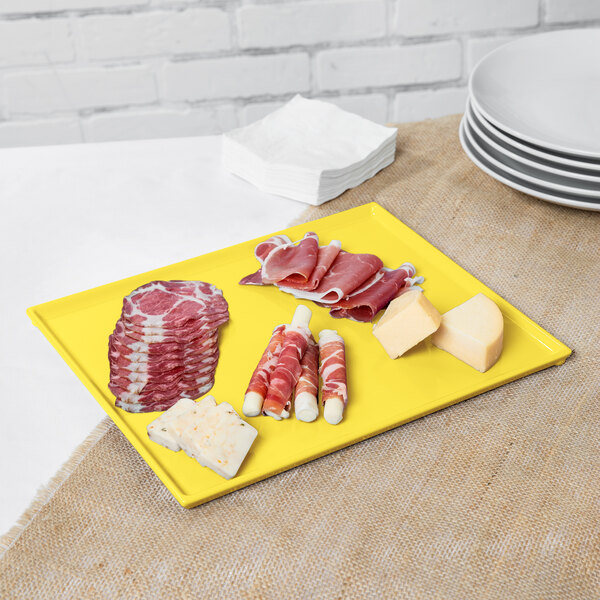 A yellow Tablecraft rectangular cooling platter with cheese, meat, and crackers.
