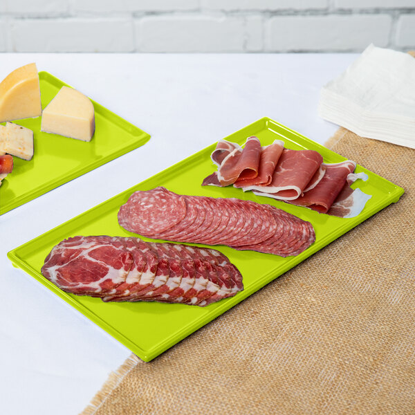 Two lime green Tablecraft metal trays with meat and cheese on them.
