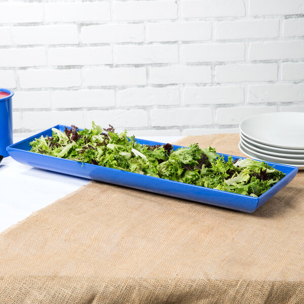 A blue rectangular Tablecraft tray with green lettuce on it next to a blue mug.