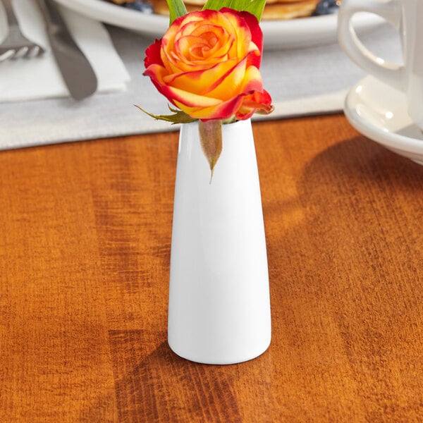 An Acopa bright white porcelain bud vase with a yellow rose in it on a table.
