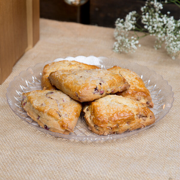 A Fineline clear scalloped plastic catering tray with pastries on a table.