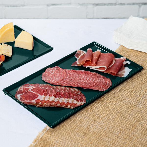 Two Tablecraft Hunter Green cast aluminum rectangular cooling platters of meat and cheese on a counter.