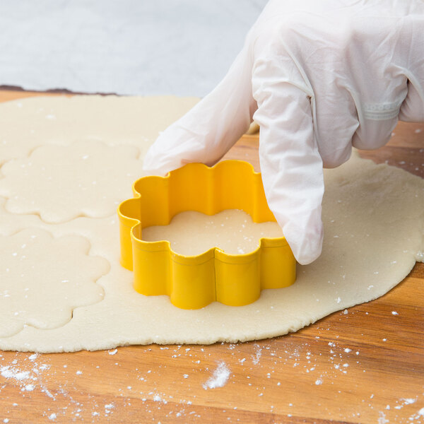 A person wearing gloves using a Wilton metal flower cookie cutter to cut out cookies.